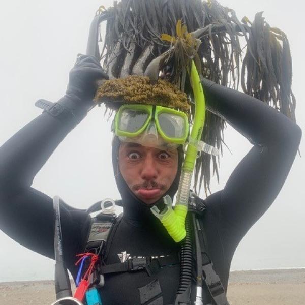 Man in wetsuit lifting a mass of kelp above his head