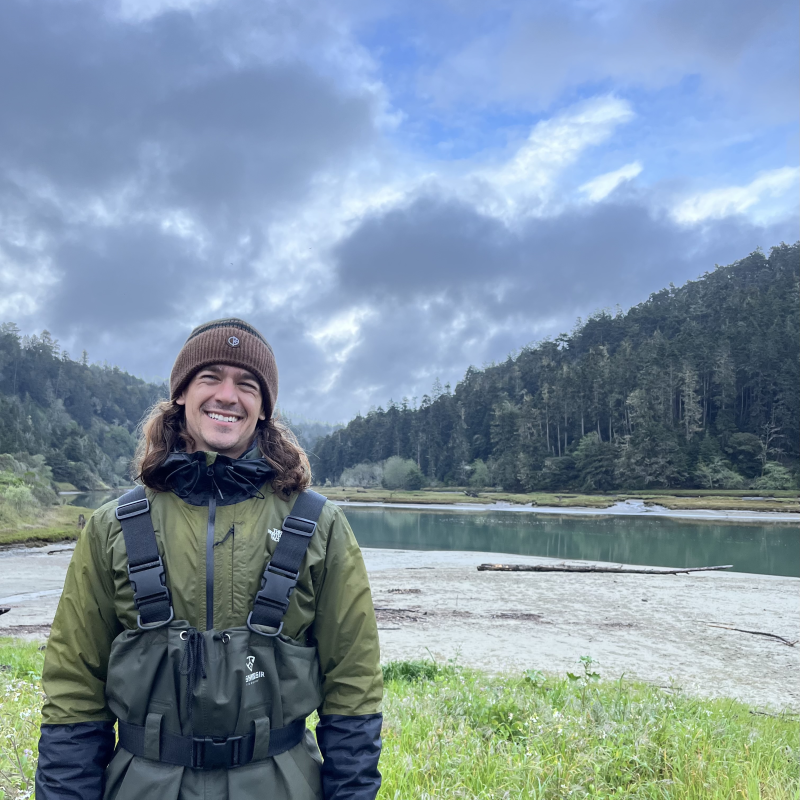 Person standing at a lake's edge with forest line in the background