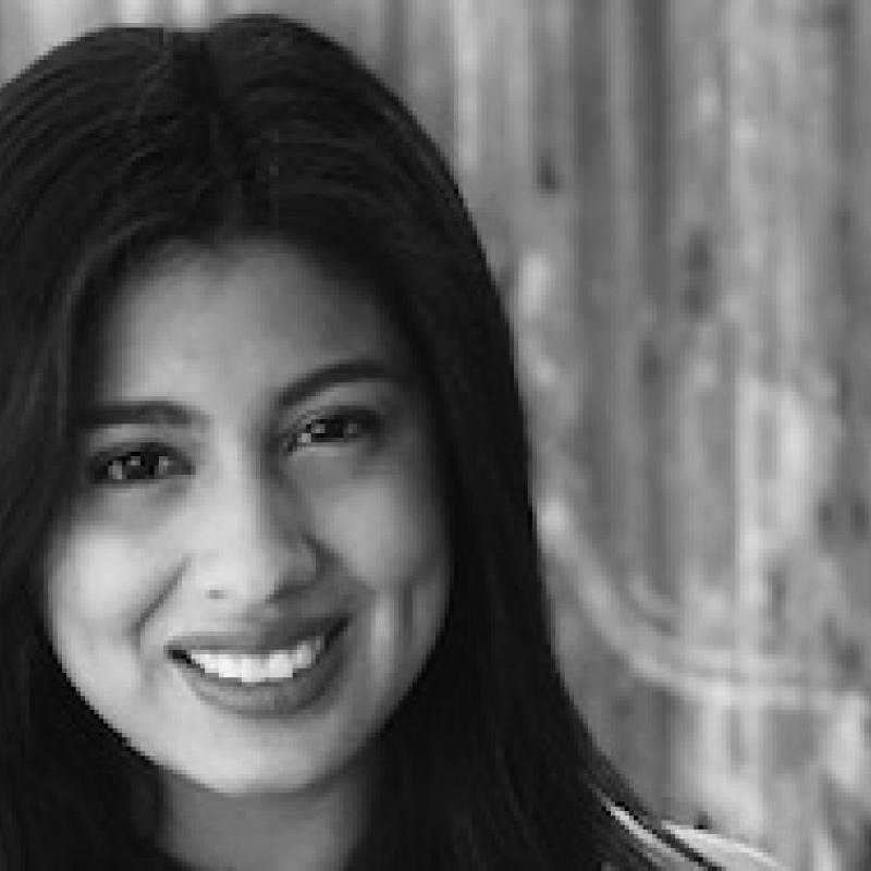  Jem Morales' black and white headshot in front of a wooden background.